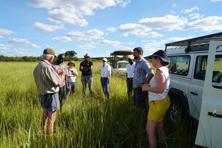 Allan Savory and group standing next to a Land Rover in tall green grass with blue sky
