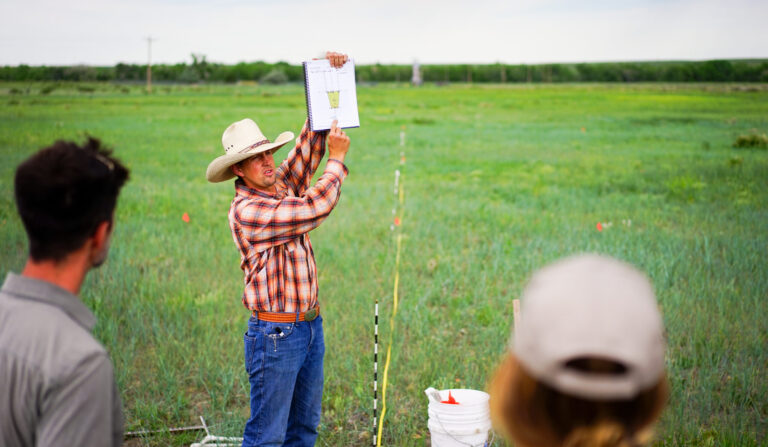 An EOV Verifier holding up a clipboard in a field while a group watches